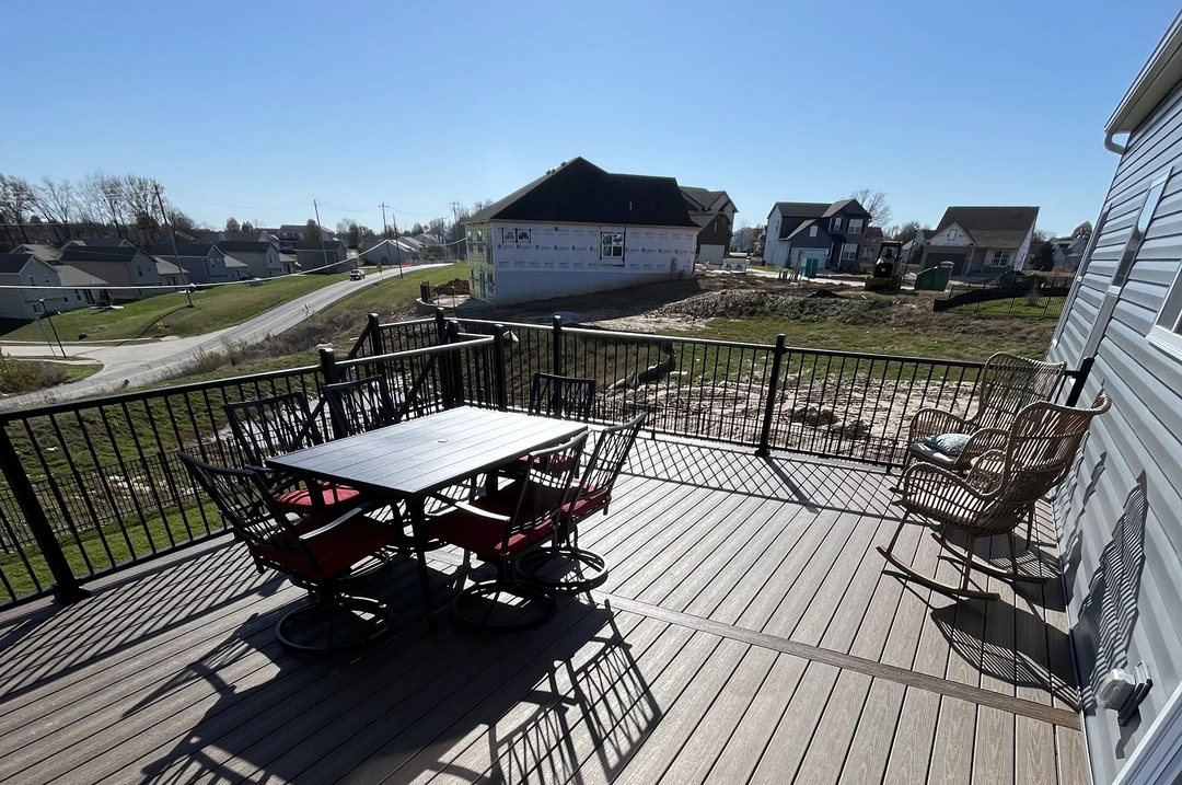 93402.99117641538 A brown deck with a black outdoor dining set with red cushions and two wicker rocking chairs in the sun.